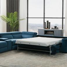 Blue velvet designer corner sofa next to a large green plant and huge glass windows