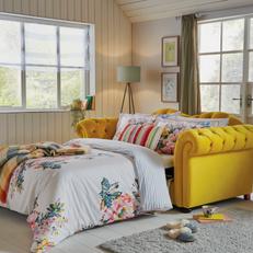 Yellow Chesterfield sofa bed in a bright living space with white bedding with flowers on