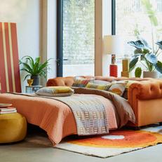 Orange chesterfield velvet sofa in a bright colourful living room with orange and colourful bedding