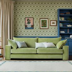 4 seater green sofa with white piping next to a green patterned wall with blue panneling and pictures