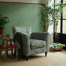 Green floral accent chair with gold piping and walnut feet next to a green floral wall 