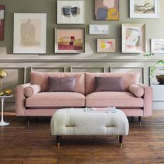 Light pink sofa with a white boucle footstool next to a wall full of picutres and prints