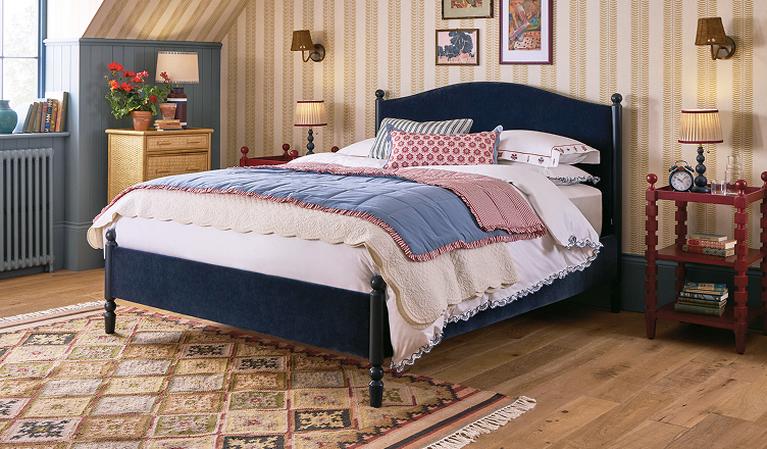 Navy velvet bed with wooden detail against a striped wallpaper wall
