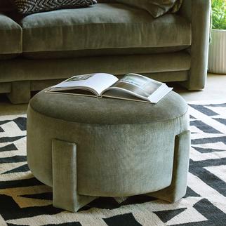 Dark green round footstool on a monochrome patterned rug with a magazine sat upon it
