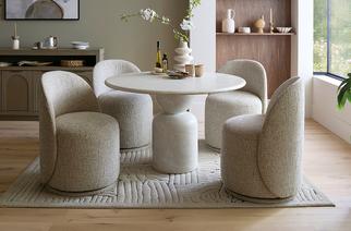 Cream marble effect round dining table with 4 fabric light grey dining chairs next to a modern wooden sideboard with gold handles