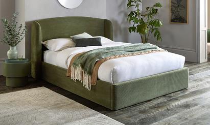 Olive green divan bed with green bedding and throws surrounded by plants
