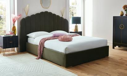 Dark green velvet bed with a pink throw next to black bedroom furniture and large windows