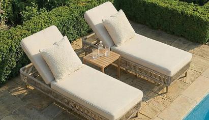 Beige rattan sun lounger with a wooden table next to an outdoor pool