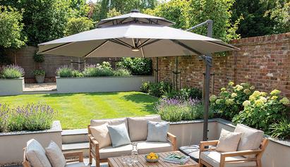 Large grey parasol in a summery garden full of plants and grene grass with wooden garden furniture