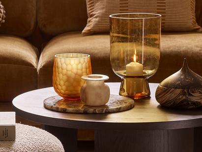 Candles and marble accessories on a round walnut tablr next to a brown sofa