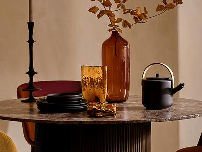 Antique glassware in black and orange on a round dark brown marble dining table next to an orange dining chair