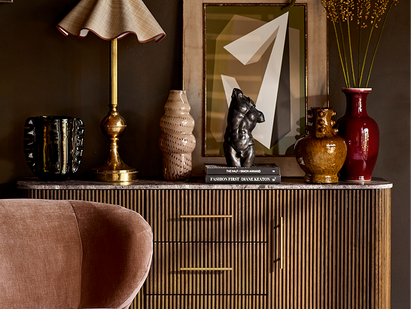 Dark and moody room with a walnut panelled sideboard with marble top, finished with a gold and cream lamp, black vases and a neutral artwork