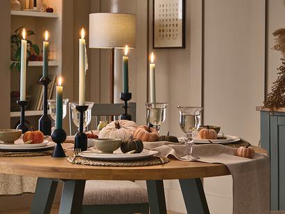 Sage green and wood dining table and chairs set with halloween themed table decor of candles, pumpkins and linen