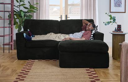A man in a pink shirt and white trousers laid on a black sofa 