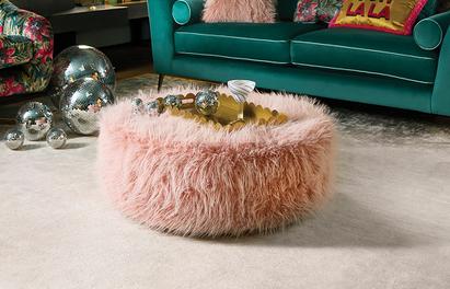 Pink fluffy round footstool next to a velvet teal sofa
