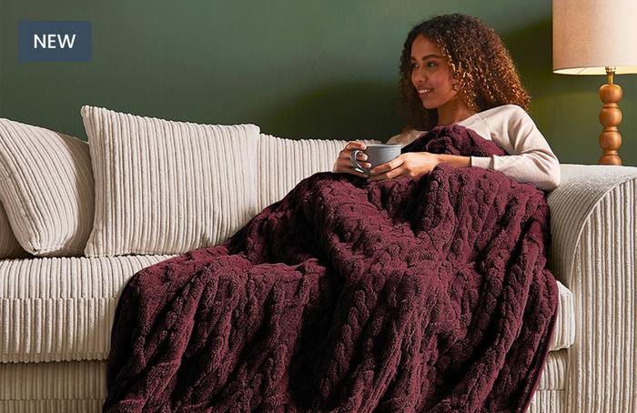 A young women curled up on a cream cord sofa with a hot drink and a luffy burgandy heated throw