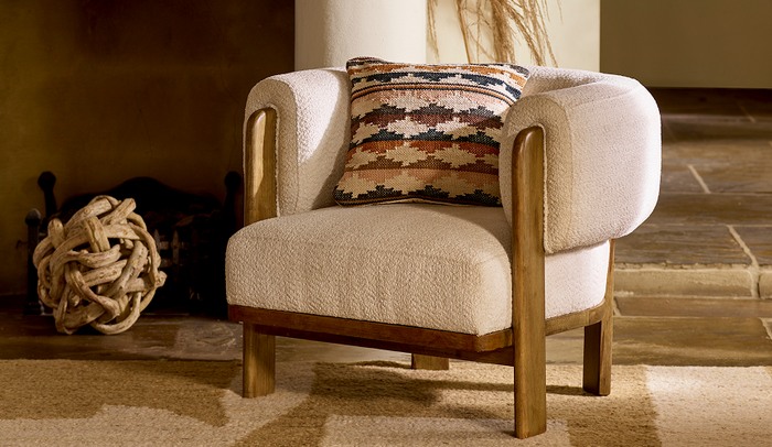 White boucle accent chair with oak arms and feet on a wooden floor with a brown patterned scatter cushion