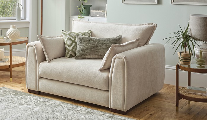 Cream cuddler sofa with green patterned scatter cushions next to a sage green wall and rug