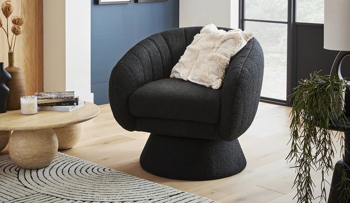 Black boucle swivel chair next to a blue wall and a marble effect coffee table finished with a white fluffy cushion