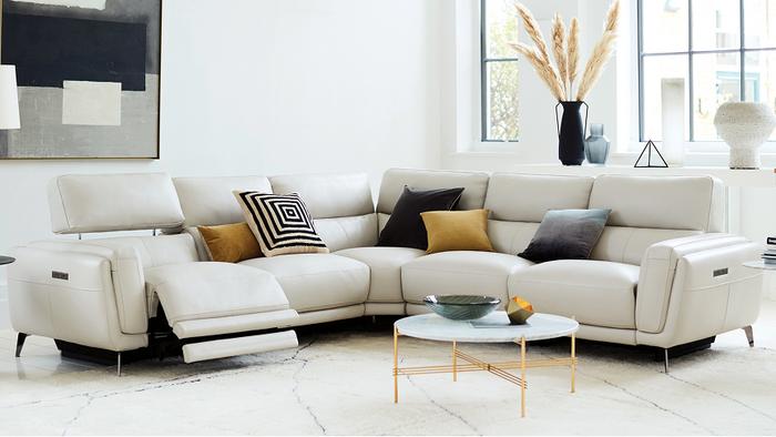 White leather recliner corner sofa with black metal legs in a bright living space with yellow and monochrome scatters and accessories