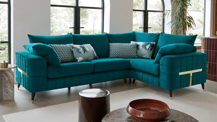 Teal corner sofa with gold bar detail on the arm with matching floral and geometric scatter cushions next to large windows