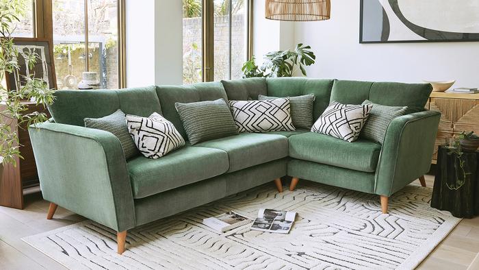 Sage green mid century corner sofa on wooden legs sat upon a monochrome pattern rug in a bright large living space