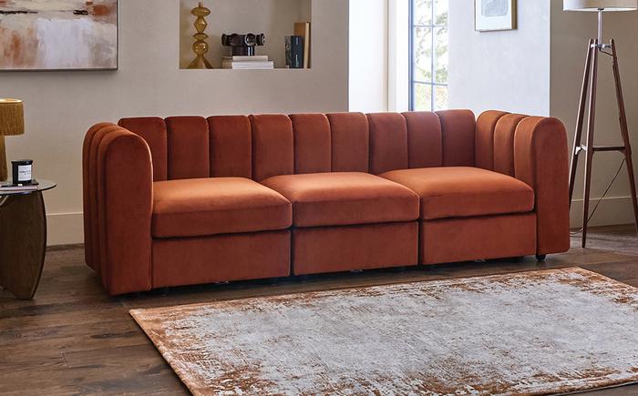 Rust orange curved modular sofa next to a orange patterned rug and a dark wood floor