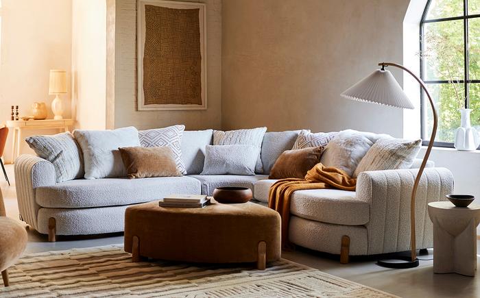 Boucle curved sofa with wooden feet and a curved brown footstool in a cosy living space with beige accents 