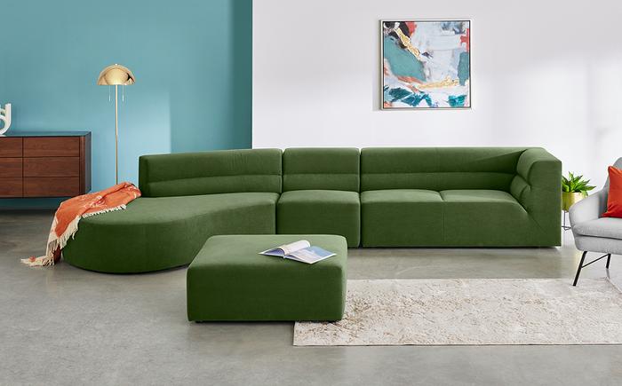 Retro style modular curved sofa in green next to a blue and white wall with a square matching footstool