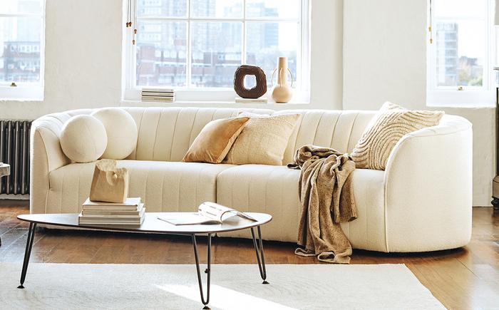 Cream curved sofa with fluting in a bright living space with neutral scatters and accessories