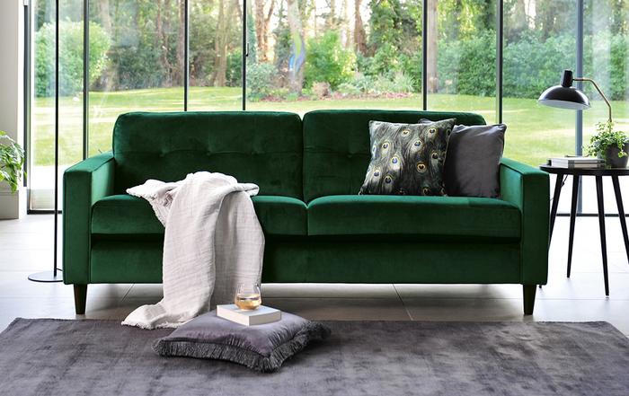 Green velvet sofa next to a large window with a white throw