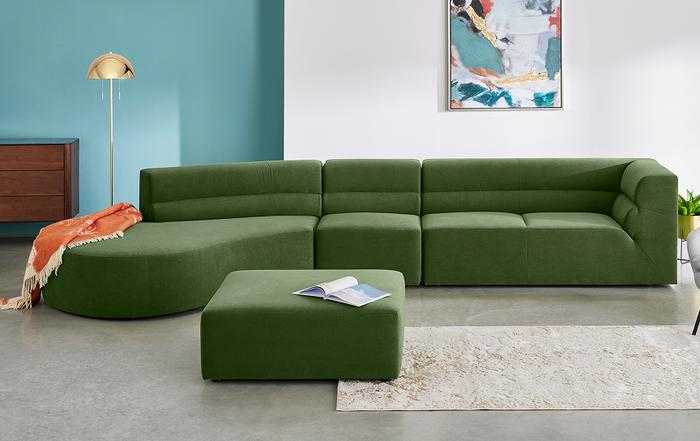 Green curved sofa with a matching square footstool next to a white and blue wall with cream rug