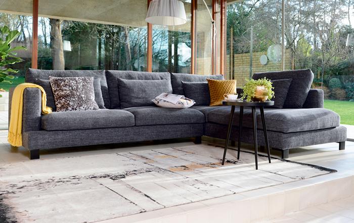Dark grey corner sofa next to a large open window  with colourful scatter cushions