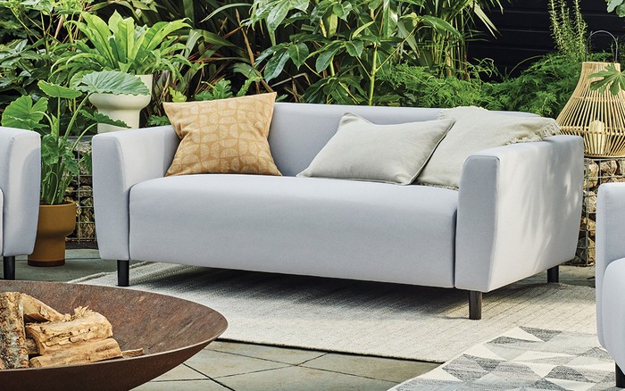 light grey garden sofa with patterened scatter cushions on top a beige outdoor rug