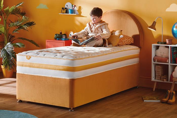 A young boy sat reading on a Silentnight Healthy Grow Mattress on a orange bed