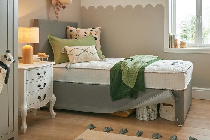 A single bed with green throw and pillows next to a white chest of drawers