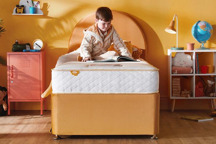 A young boy sat reading on a Silentnight Snooze Mattress on a orange bed