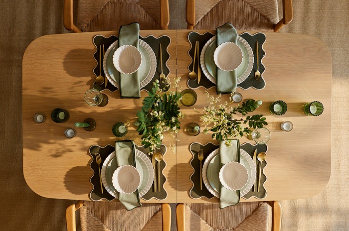 Top level view of a wooden dining table with sage green place holders and bowls with tea lights in a green golder