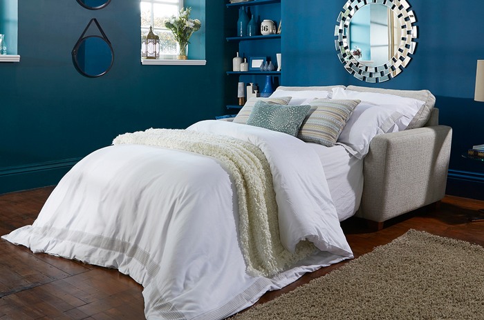 House Beautiful Sophia sofa bed next to a dark blue wall with blue and white bedding and cushions