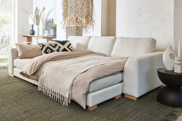 Calix sofa bed in white with light oak feet, with a monochrome scatter cushion, neutral throw in a bright living space