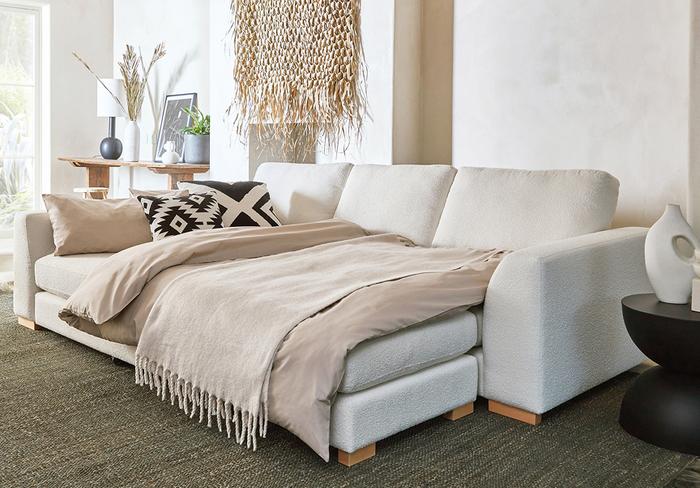 White boucle sofa bed with oak wooden feet with monochrome bedding and a neutral frayed throw