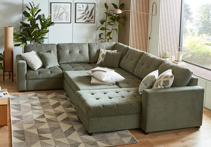 Sage green buttoned sofa bed with patterned green rug next to a pale green wall with wooden panelling