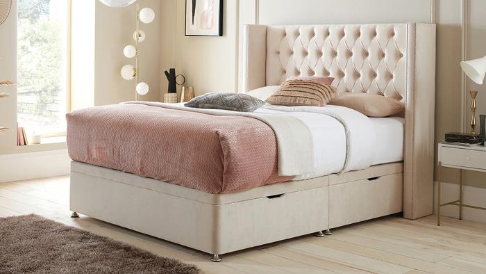 Cream buttoned divan bed with pink bedding and a throw in a neutral bright bedroom