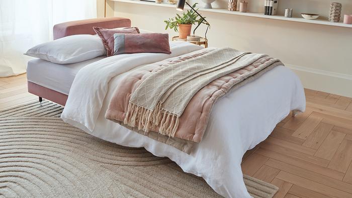 Pastel pink sofa bed with white bedding and pastel pink and neutral throw