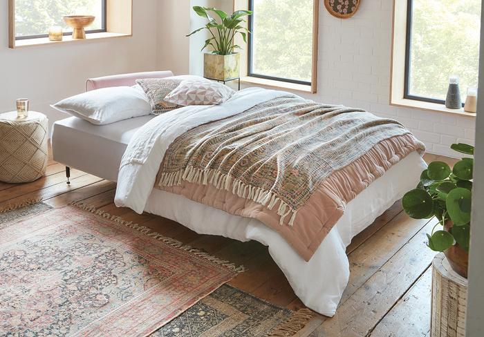 Blush pink sofa bed with pastel pink and neutral bedding next to a pink patterned rug