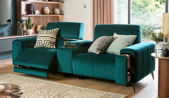 Green velvet recliner sofa on a wooden floor with a varity of patterned scatters with a wooden feature wall