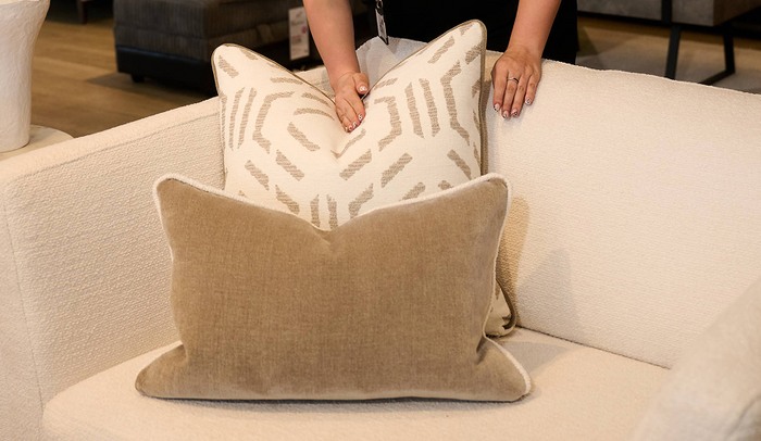 A womens hand smooth and plumping up two neutral scatter cushions on a sofas