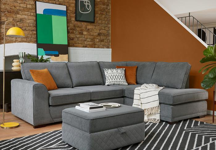 Dark grey corner sofa with quilted arm detail finished with orange and monochrome scatter cushions sat next to an orange wall and monochrome rug