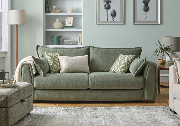 Sage green sofa next to a pale green wall with green patterned scatter cushions and a footstool