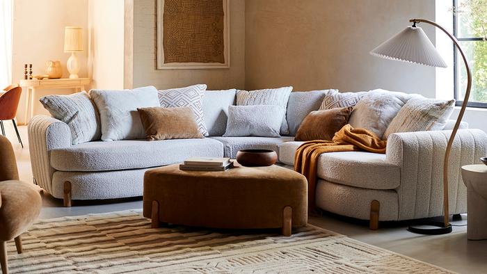 Boucle corner sofa with wooden feet with a triangle brown footstool in a cosy living space